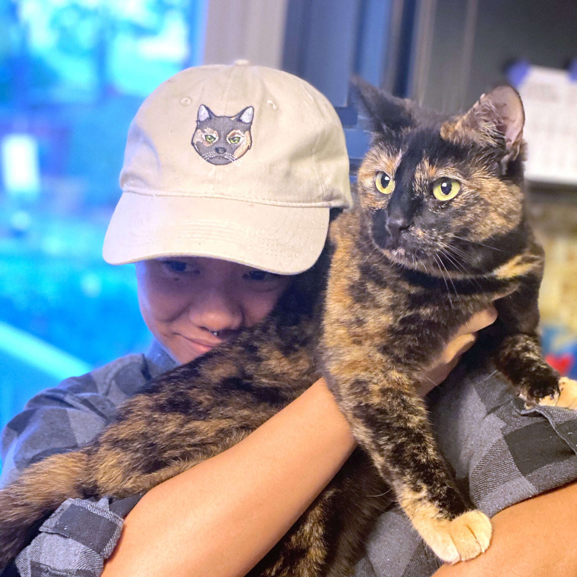 Khaki dog dad hat with a cat embroidered on it on a cat mom holding her cat.