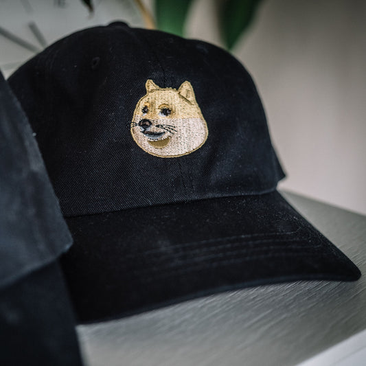 Doge Dad Hat in black sitting on a ledge with a closeup view of the embroidery details on the front of the hat.